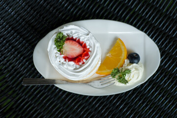 Strawberry Cake White cream on a plate decorated with oranges and blueberries. placed on a black woven table