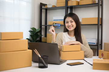 Shopping online. Young asian woman holding credit card for shopping payment. Buy item online delivery at home. Small business entrepreneur with many parcel box on table