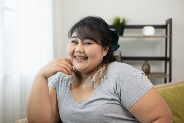 Naklejka premium Happy women's plus sitting on sofa in living room. Body positive plus size female lives happily and is proud of herself.
