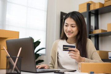 Shopping online. Young asian woman input the serial number of credit card to laptop for shopping payment. Buy item online delivery at home. Small business entrepreneur with many parcel box on table