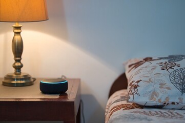 Personal assistant smart speaker on a wooden table with table lamp in a bed room and copy space for...