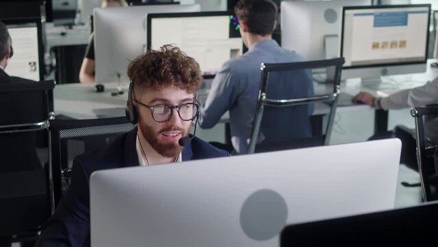Call Center Office: Portrait of Friendly Caucasian Male Technical Customer Support Specialist Talking on a Headset, Diverse group of workers talks on sale hotline. Busy seller at agency office indoor