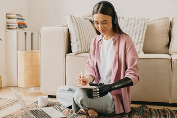 Young attractive cyberlady with artificial robotic bionic hand smiling while taking notes listening...