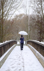 Candamia park snowy day in winter girl walking across a wooden bridge with her photo camera and holding an umbrella, Leon Spain