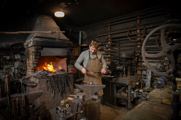 The blacksmith manually forging the red-hot metal on the anvil in smithy with spark fireworks - obrazy, fototapety, plakaty