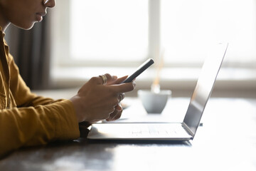 Digital devices on office workplace table of young African American business woman. Close up of gadgets. Millennial professional texting online message on mobile phone at laptop computer
