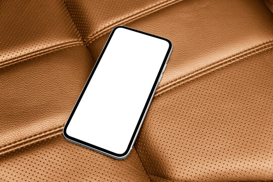 Smartphone in a car use for navigate or GPS. Driving a car with smartphone. Mobile phone with isolated white screen on brown perforated leather seat. Copy space. Empty space for text.