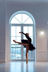 Acrylglasbilder Tanzschule ballerina in black against  background of large window with an arch  © Anna