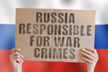 The phrase " Russia responsible for war crimes " on a banner in men's hand with blurred Russian flag on the background. Battle. Deaths. Killings. Conflict. Combat. Confrontation. Moscow. Assault