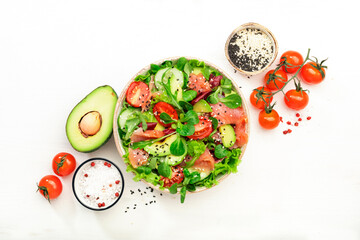Spring salad with salted salmon, avocado, tomatoes, cucumber, black sesame seeds, olive oil, and mixed herbs. White background, top view, copy space