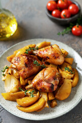 Baked chicken legs and potatoes with oranges, garlic and onions in a plate on a dark culinary background closeup