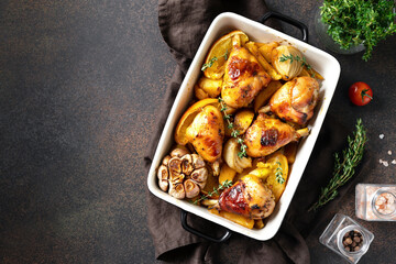 Baked chicken legs and potatoes with oranges, garlic and onions in a baking dish on a dark culinary background. Top view from the copyspace