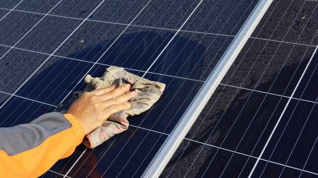 Hand Cleaning Solar Panels. A Woman's Hands Use A Towel To Wipe Dirty And Nasty Solar Panels With Dust And Bird Droppings Outdoors With Copy Space. Selective Focus