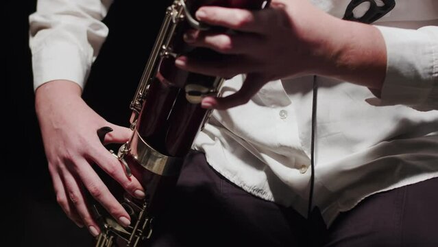 Woman plays bassoon music sitting on chair in studio, front view. Female musician sits on chair and plays wind instrument