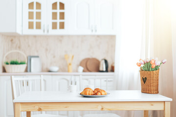 On wooden table croissants with flowers in front of the kitchen.