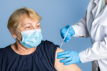 The woman came to receive another booster dose of the vaccine. The doctor makes an injection in the forearm of an elderly woman.