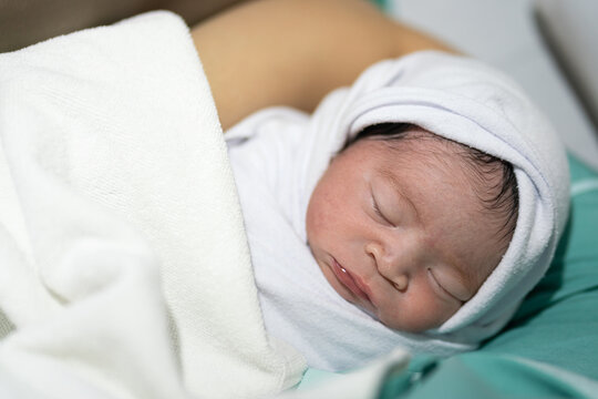 Cute infant Caucasian newborn baby which is sleeping on mother's embrace, baby portrait close-up photo.