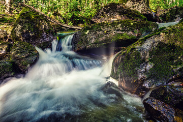 Beautiful river with flowing water, rapids, rocks moss and forest in background, long exposure in volda, norway