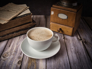 frischer Kaffee vor alten Büchern und einer alten Kaffeemühle