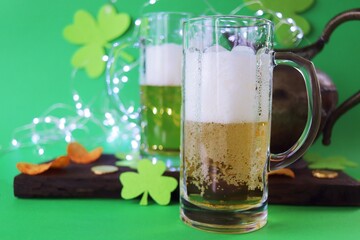 St. Patrick's Day, fresh beer in glass mugs, gold coins, shamrocks and illuminations on a bright green background, party, congratulations, postcard