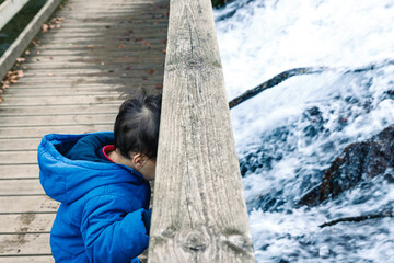Petit garçon regardant un cours d'eau sur un pont de bois