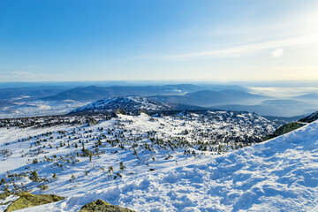 View from mount peak to mountain hills, white snow, blue sky, stones and fir trees. Winter landscape in Gornaya Shoria, Sheregesh ski resort in Russia, Altai mountains nature background.