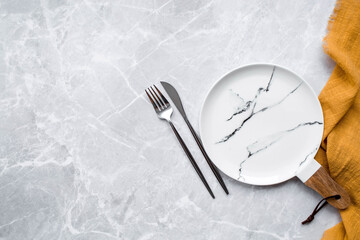 Banner. An empty ceramic marble plate with a wooden handle, a fork, a knife and a towel against the background of a gray concrete table. Space for text. Menu concept for cafes and restaurants.