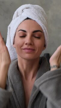 Young woman at home in the bathroom in a bathrobe with a towel on her head cheerfully sends kisses to the camera, vertical frame 