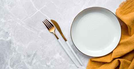 Banner. An empty ceramic plate, fork, knife and towel against the background of a gray concrete table. Space for text. Menu concept for cafes and restaurants.