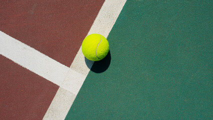 Yellow tennis ball lying on line of the red and green court. Flat lay view. Space for text
