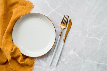 Banner. An empty ceramic plate, fork, knife and towel against the background of a gray concrete table. Space for text. Menu concept for cafes and restaurants.