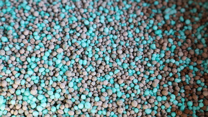 Mixed chemical fertilizer granules background. Abstract texture of primary mineral granules containing N (nitrogen), P (phosphorus) and K (potassium) for use in agricultural farms. Selective focus