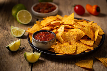 Single big black plate of yellow corn tortilla nachos chips with salsa sauce over wooden table - obrazy, fototapety, plakaty