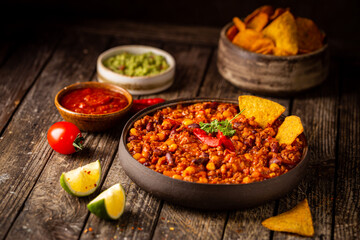 Mexican hot chili con carne in a bowl with tortilla chips on wooden background