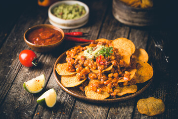 Delicious plate of yellow corn nachos chips with cheese, minced meat and red hot spicy salsa over wooden table