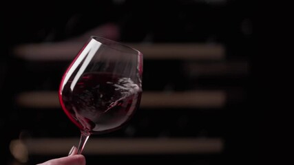 Red wine. Close up of female hand swirling the glass to make the wine spinning. Slow motion video.