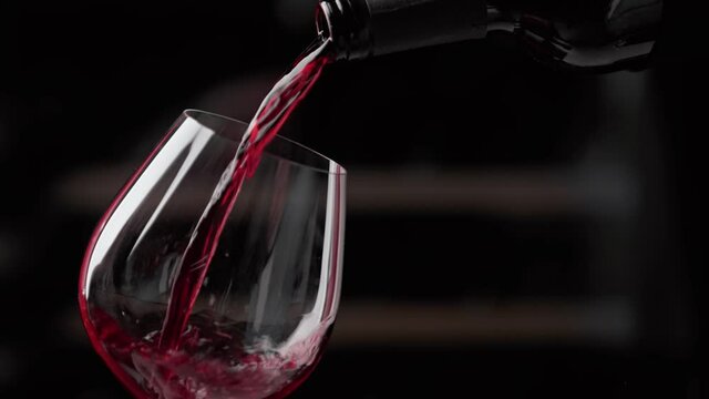Pouring red wine to glass. Slow motion video.