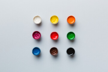 jars with gouache of different colors on Colored background. hobby painting. Top view with empty...