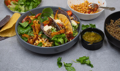Vegan Mexican taco bowl consisting of corn, lentil, vegan cream, greens, pickles