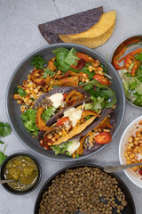 Vegan Mexican taco bowl consisting of corn, lentil, vegan cream, greens, pickles