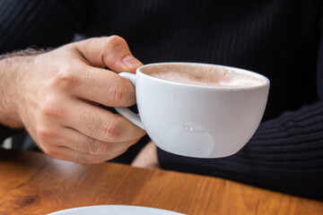 Man holding a cup of coffee white sitting in a cafe.