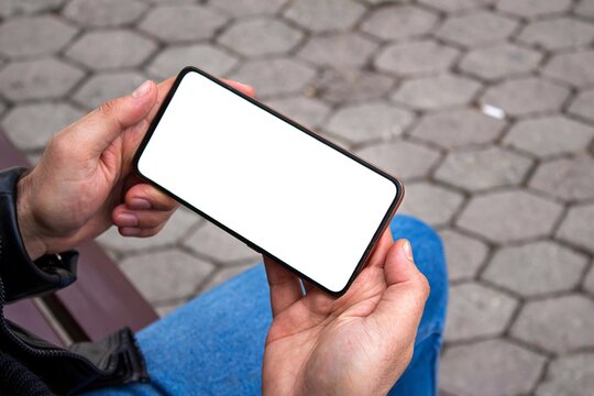 Man Hand Holding Mobile Phone With Blank White Screen At The Outdoor.