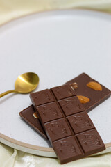 chocolate bars with peanuts, almonds and dried beans on a white plate on a white background with a gold spoon