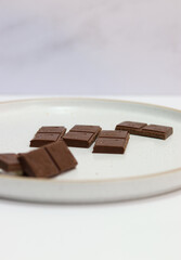 chocolate bars with peanuts, almonds and dried beans on a white plate on a white background