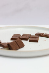 chocolate bars with peanuts, almonds and dried beans on a white plate on a white background