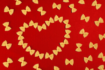 Background for Valentine's Day. Food Valentine's Day. Pasta farfalle bows in the shape of a heart on a red background for Valentine's Day.
