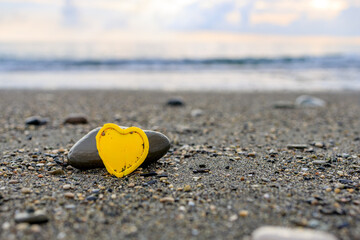 Fototapeta na wymiar yellow plastic heart on the seashore, stone and heart