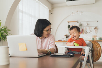 Asian mother and her son playing and laughing, Smiling Woman using laptop, Freelancer mom works from home with her cute child