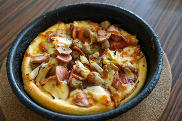 Barbeque beef pizza hut served on a black plate or bowl with a brown textured wooden table background.