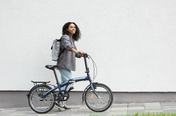 Young beautiful woman with bike over white wall background in a city, Smiling student girl with...